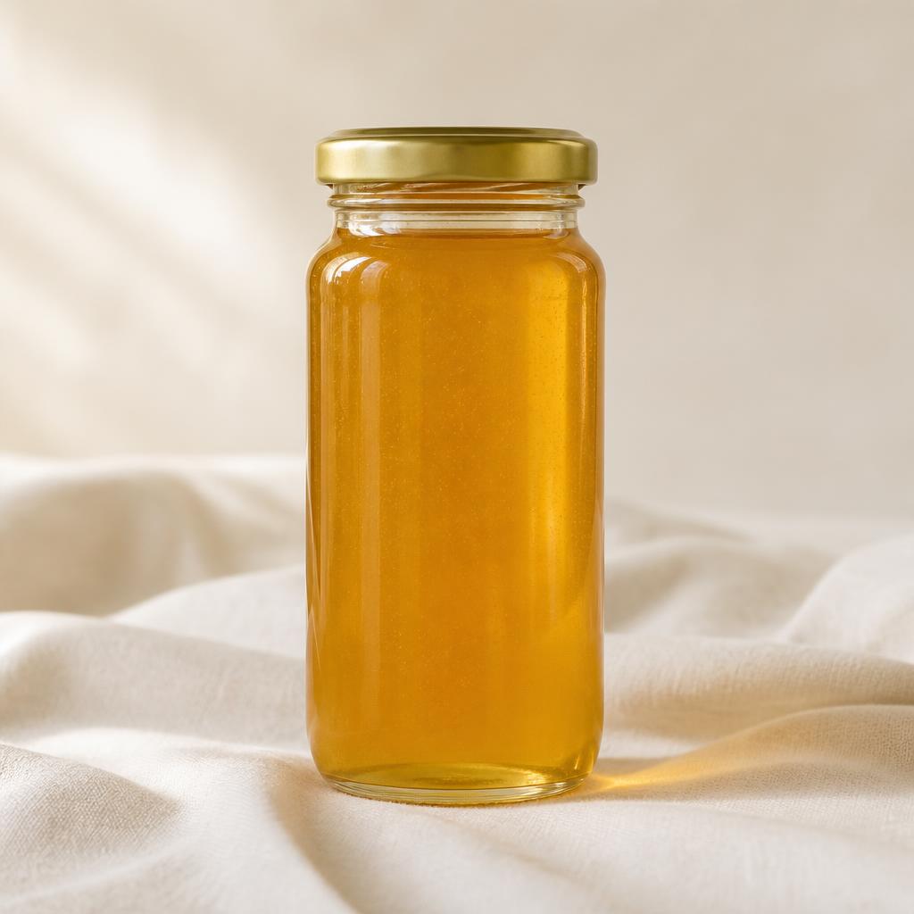 Tall 24 oz glass jar of golden honey with gold lid on cream linen